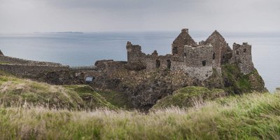 dunluce-castle-courtesy-of-lindsey-cowley Grey blue Skies with ancient stone building sitting on the edge. Green, tall grass in the foreground