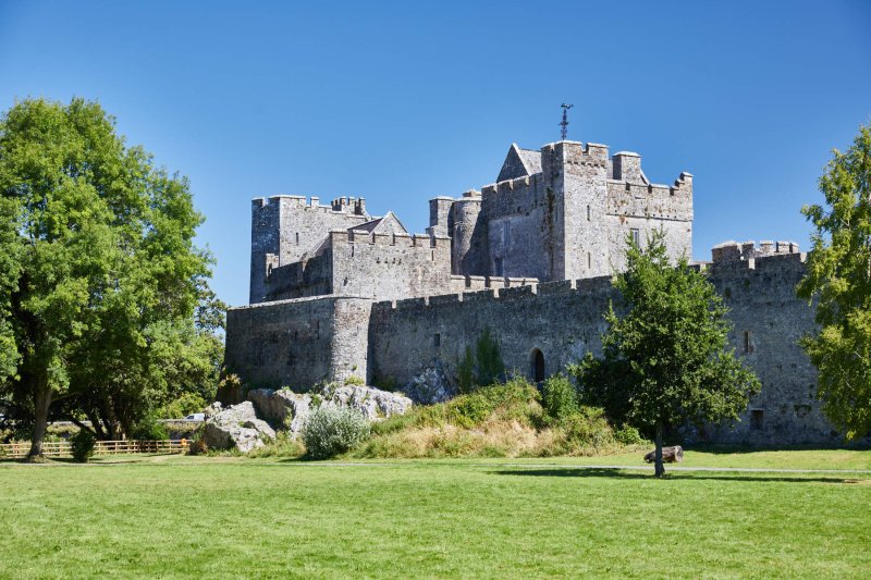 Cahir Castle, Co. Tipperary Courtesy Failte Ireland stone castle behind trees with blue sky