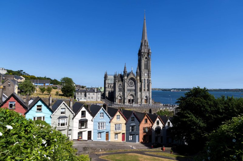 St Colmans Cathedral, Cobh pic by Chris Hall Tourism Ireland cathedral beside water behind row of colourful houses